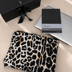 Leopard print pouch, black notebook, and silver laptop on a beige surface with a black gift box.